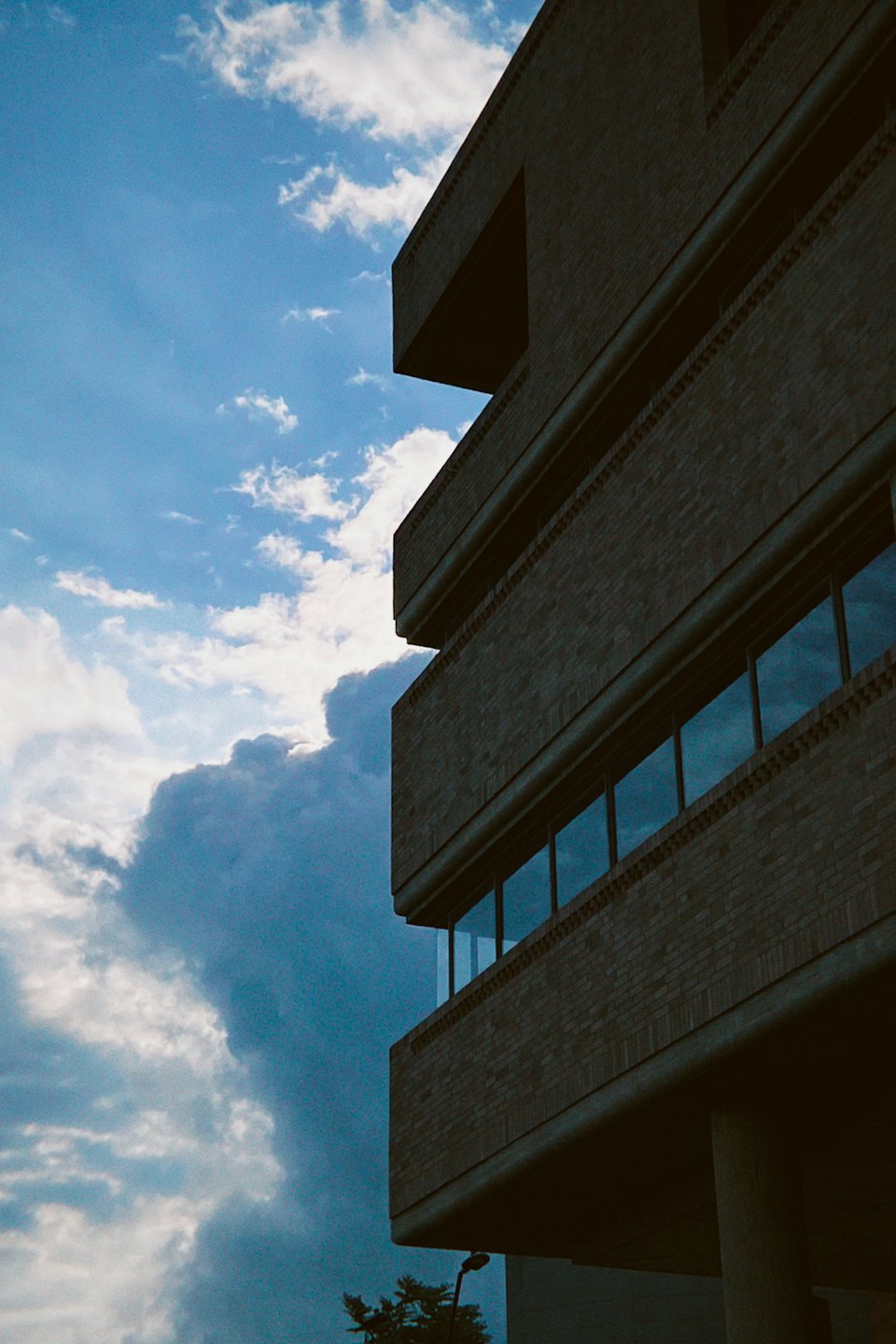 A brutalist brick building stands under a cloudy blue sky.