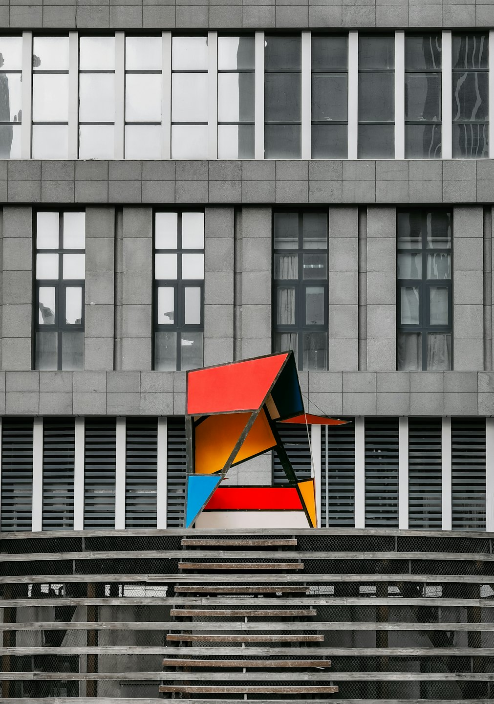 Geometric sculpture in front of a grey tiled modern building.